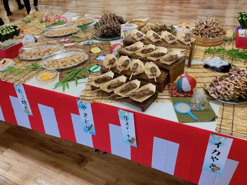 縁日風に飾り付けたテーブルに並ぶ焼き鳥やたこ焼きなどの料理