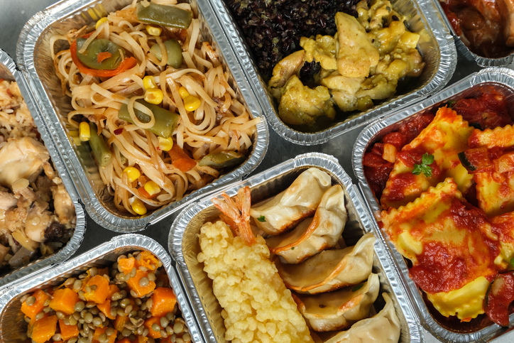 Food delivery. Different aluminium lunch box with ravioli, curry chicken rice, gyoza tempura, noodles vegetables, lentils with pumpkin . airlines meals and snacks. takeaway takeout coronavirus food