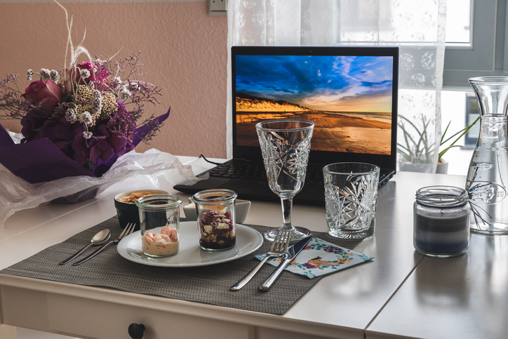 Different snacks, glass of wine, water, flowers and notebook, prepared on a table for a virtual dinner or lunch during quarantaine time because of covid-19 virus.