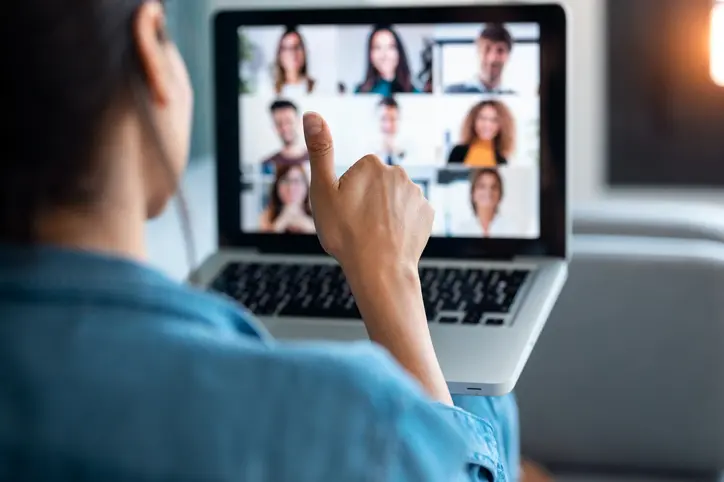 Back view of business woman making video call and showing thumb up to laptop on the online briefing while sit on sofa at home.
