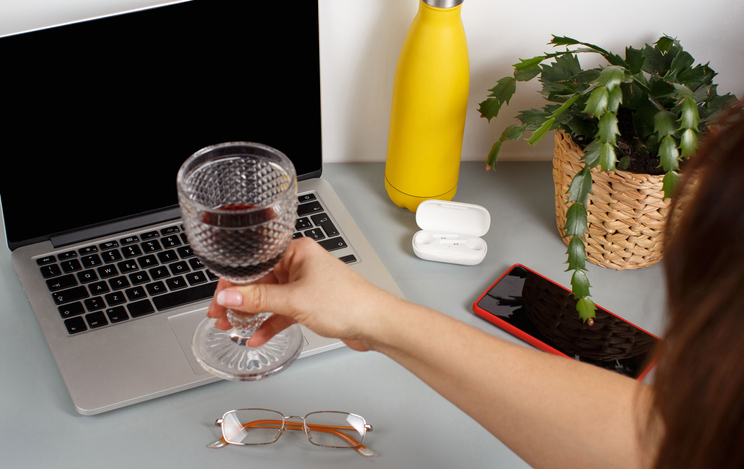 Woman hand toast with laptop with a glass of red wine. Two friends having a video call on a laptop at home, close up