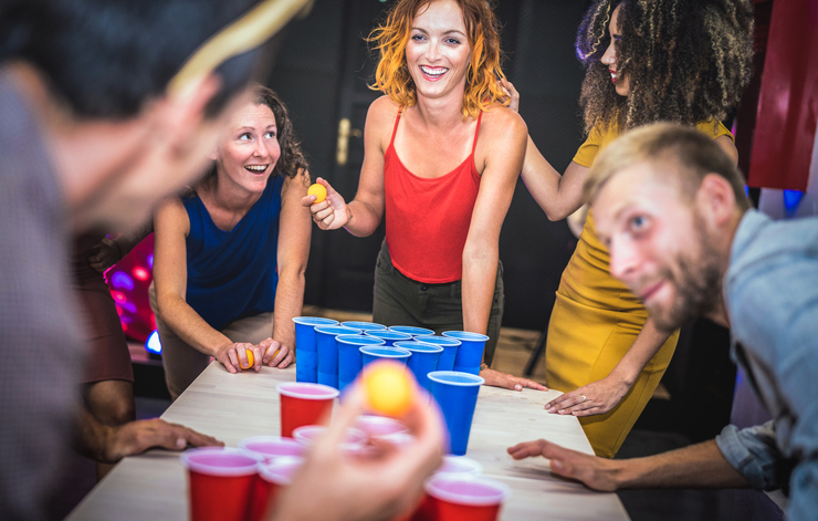 Young friends playing beer pong at youth hostel - Free time travel concept with backpackers having unplugged fun at guesthouse - Happy people on playful genuine attitude - Vivid vignetting filter