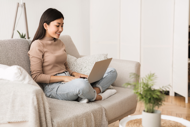 Teen Girl Surfing Internet on Laptop Computer, Sitting on Sofa with Crossed Legs, Free Space
