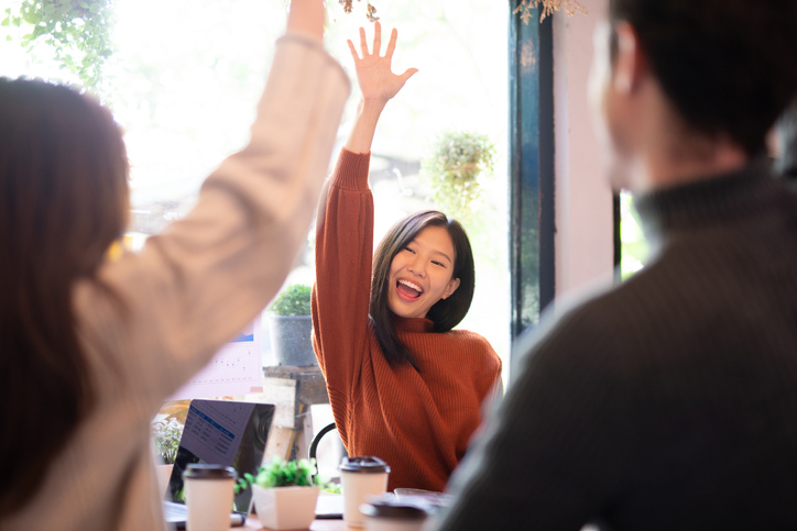 Asian woman and her team hand raised for happy winning success in coffee shop with team