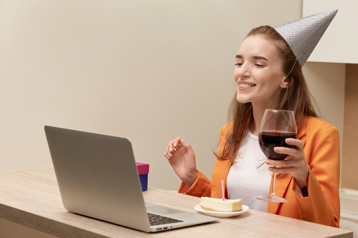 Young beautiful woman sitting at home, looking at the laptop screen with a glass of wine in her hand. Holiday online during the quarantine.